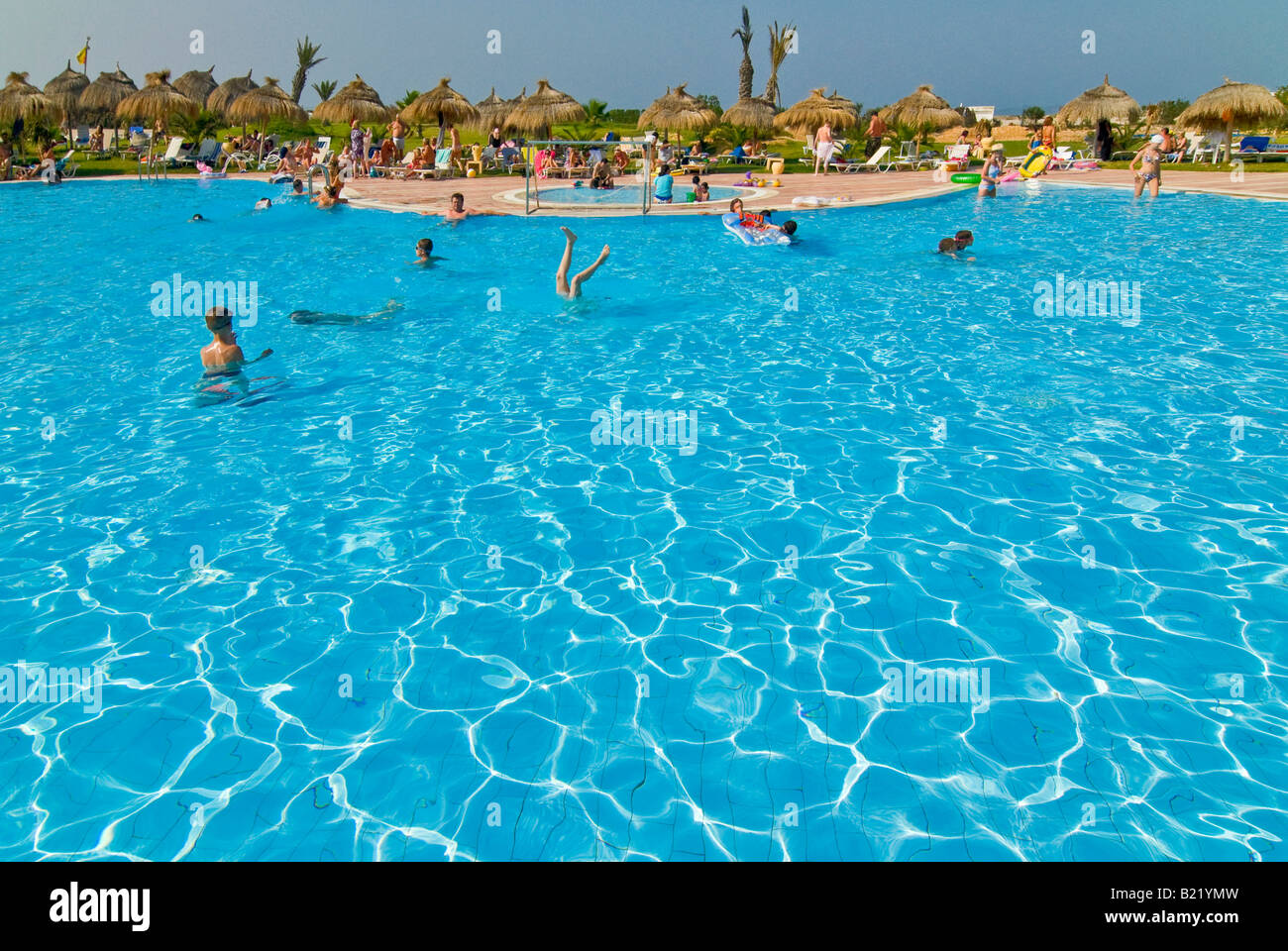 Horizontal wide angle of a busy hotel swimming pool surrounded by lots ...