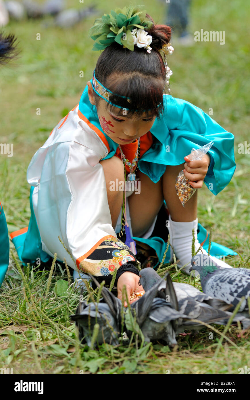 Little Japanese girl in traditional costume feeding pigeons during