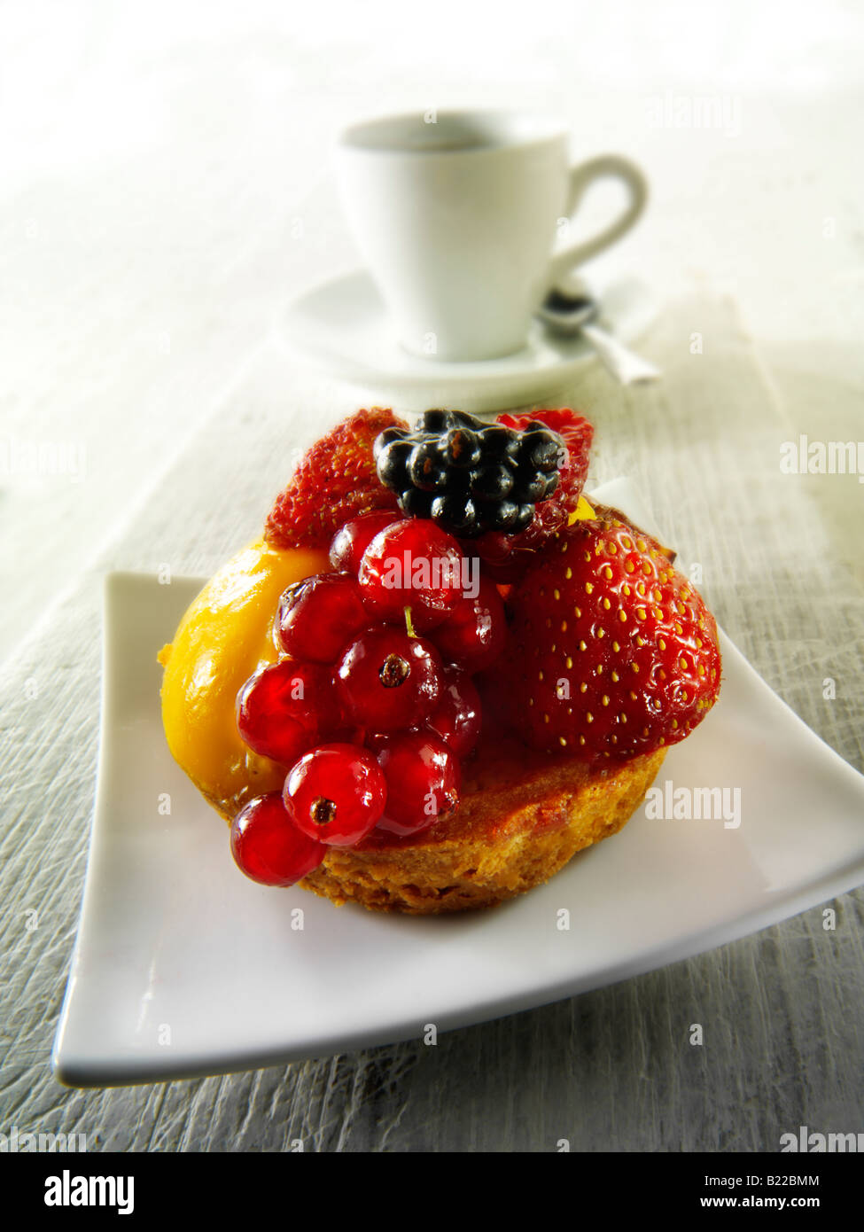 A fresh summer fruit individual sponge cake with raspberry mousse in a cafe setting with coffee Stock Photo