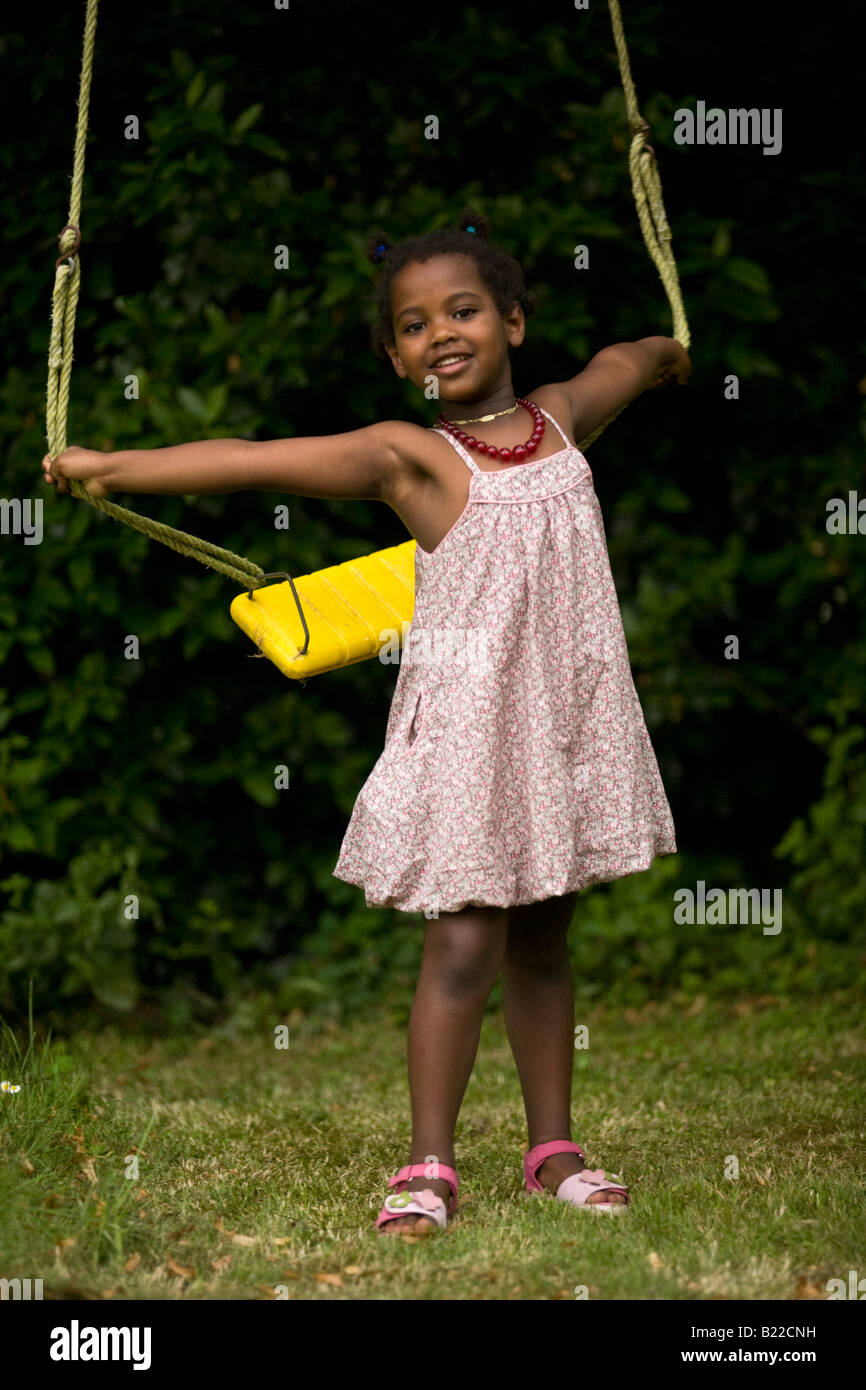 A photograph of a little black girl in front of a swing. Portrait d'une petite fille de couleur devant une balançoire. Stock Photo