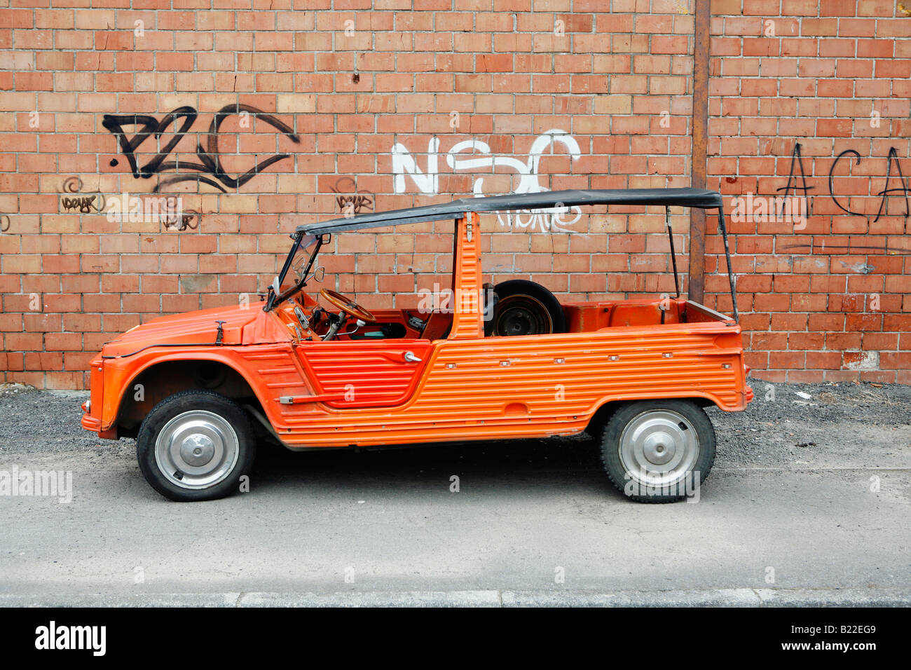 An orange red Citroen Mehari off road car stands in front of a brick wall with graffiti in Armentieres, northern France Stock Photo