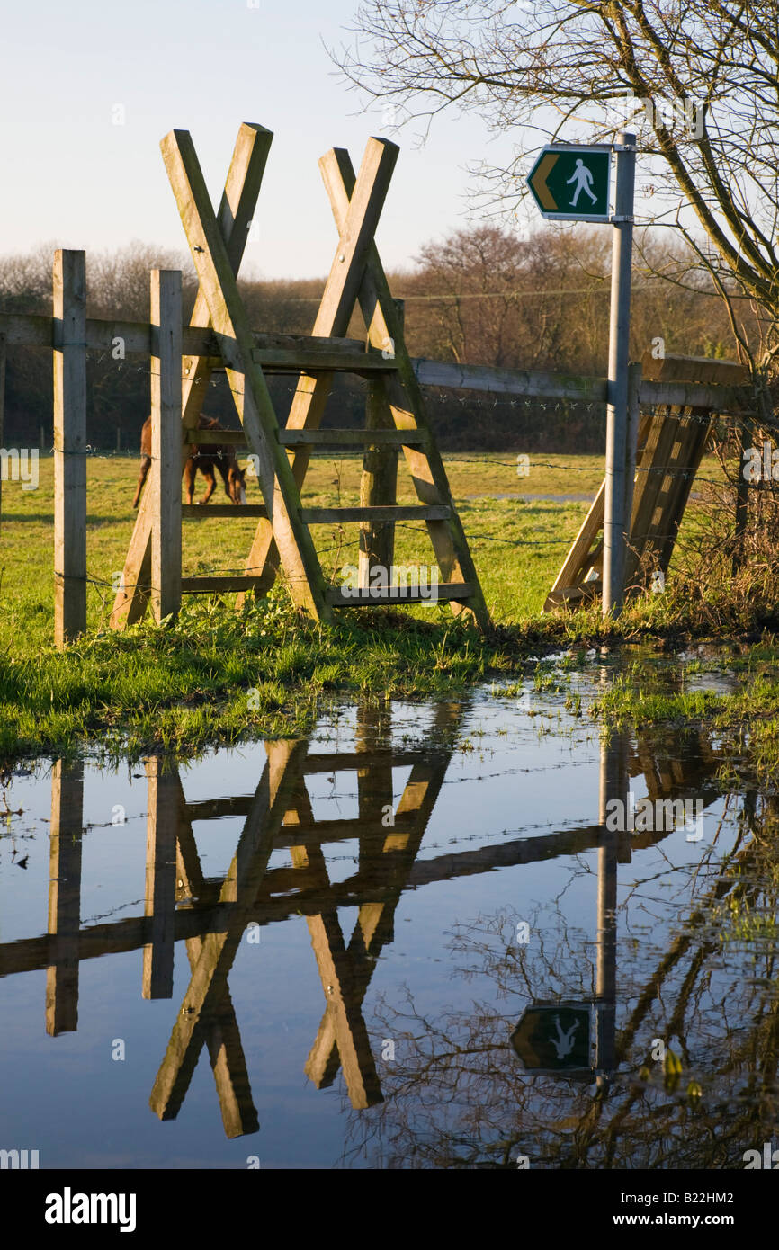 Wooden ladder stile over a fence with footpath sign reflected in a