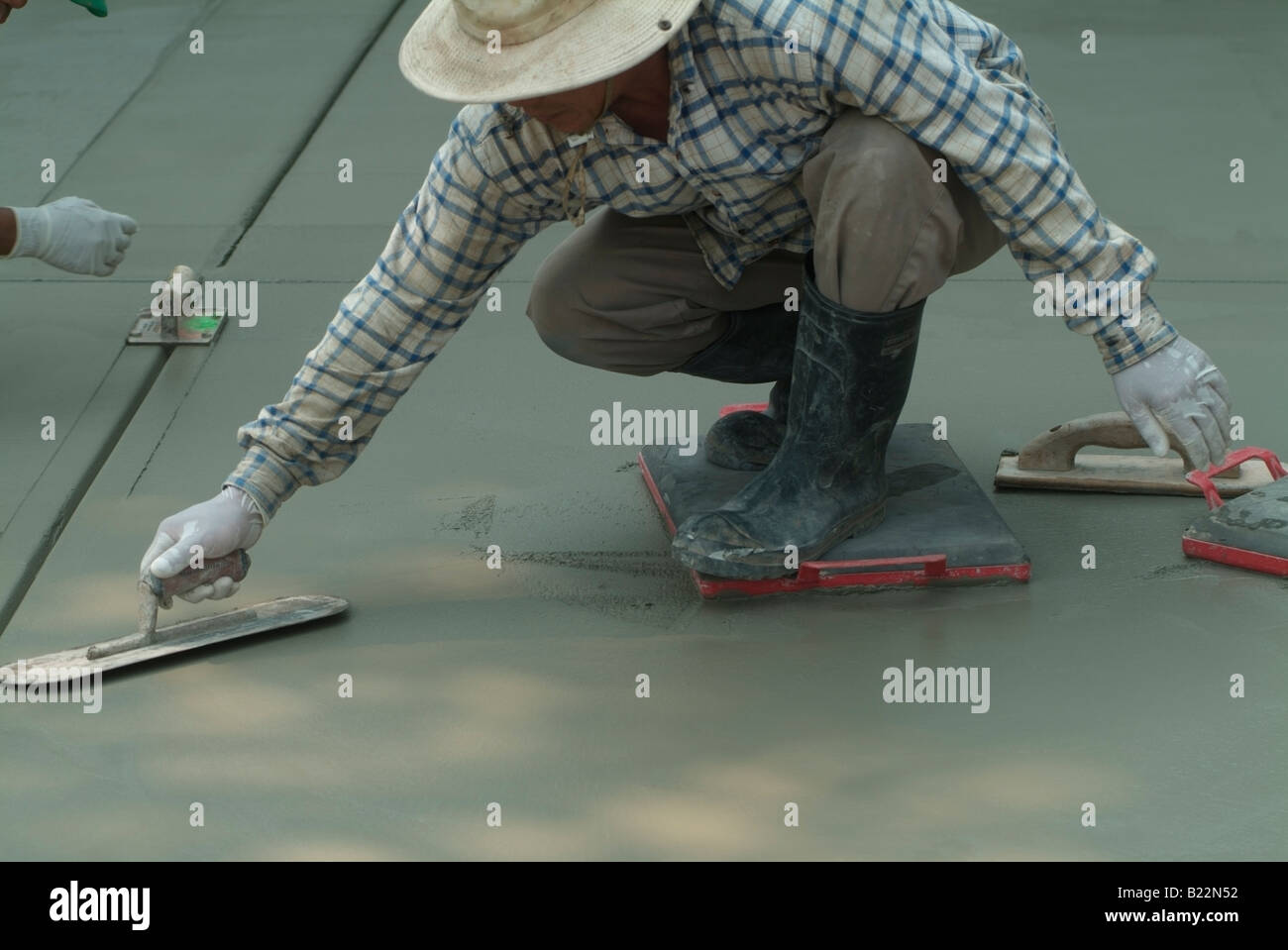 Workman leveling wet concrete with a Darby while another workman uses