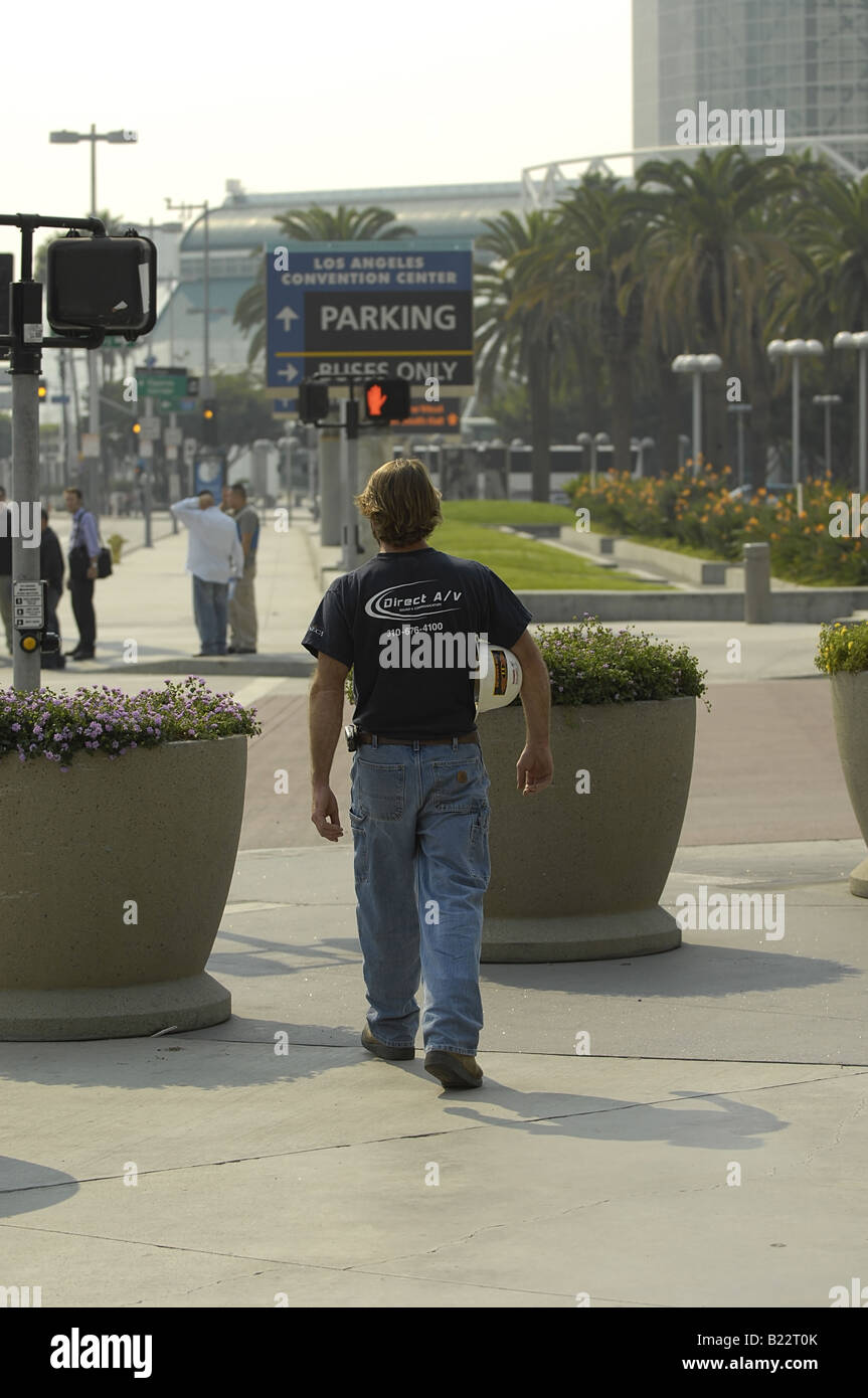 A construction worker walks along the sidewalk near the Los Angeles Convention Center carrying his hard hat. Stock Photo