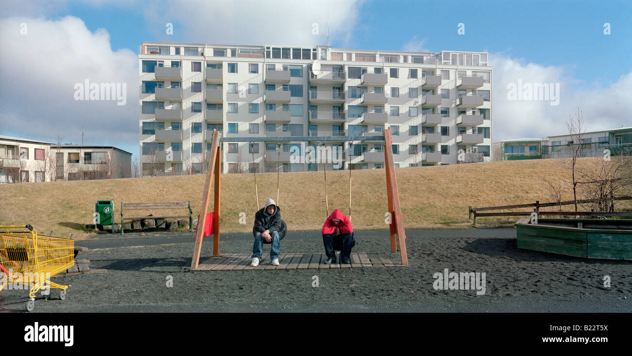 Two young men sitting on swings by an apartment block, Reykjavik, Iceland Stock Photo