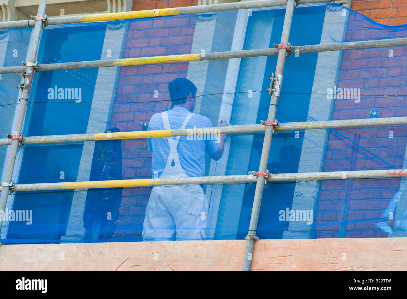 A painter decorator on scaffolding uses his mobile phone whilst painting Stock Photo