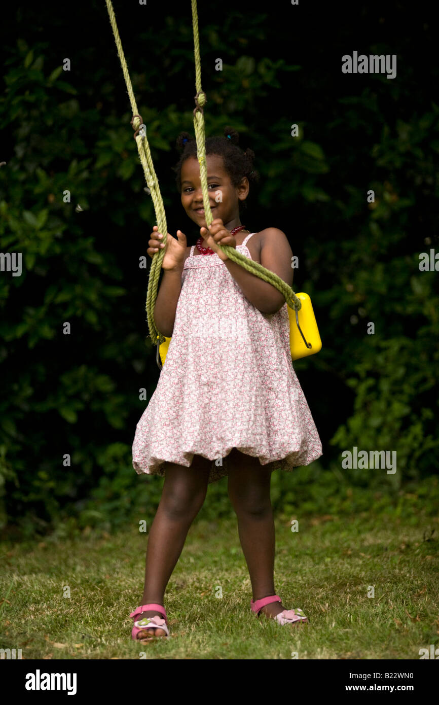 A photograph of a little shy black girl in front of a swing. Portrait d'une petite fille de couleur devant une balançoire. Stock Photo