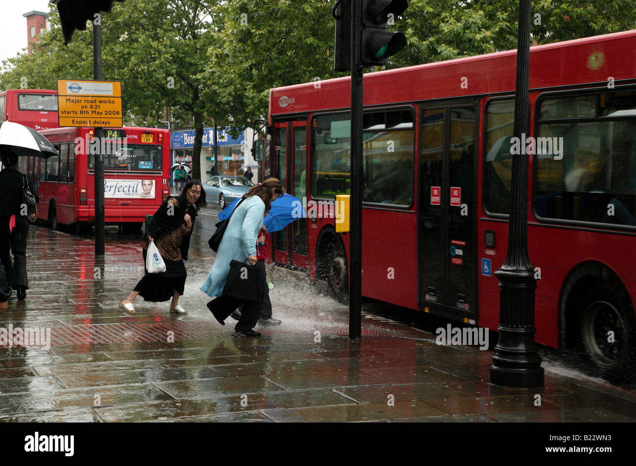 Ladies being splashed by a passing Bus whilst trying to cross at a road crossing on Lewisham High Street Stock Photo