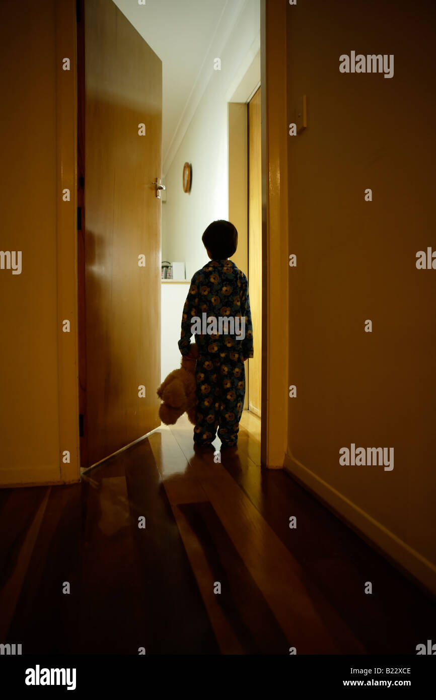 Six year old boy stands in corridor in pyjamas with teddy bear Stock Photo