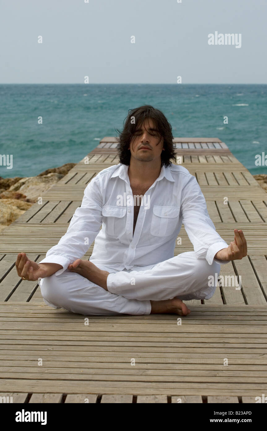 Man sitting in Yoga lotus position on a wharf by the sea Stock Photo