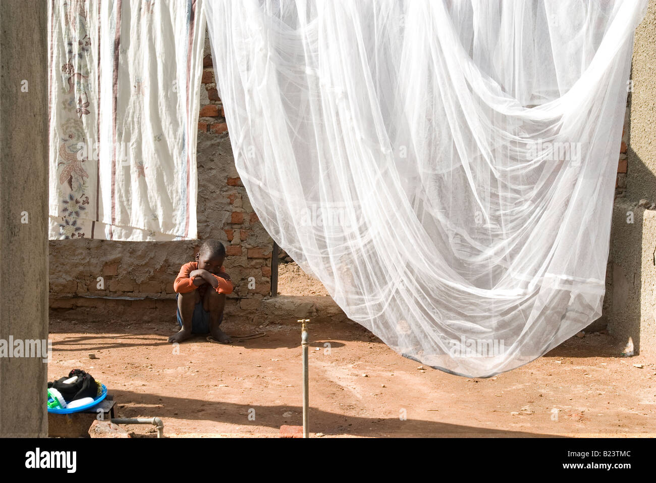 Boy sits by his mosquito net, Uganda Stock Photo