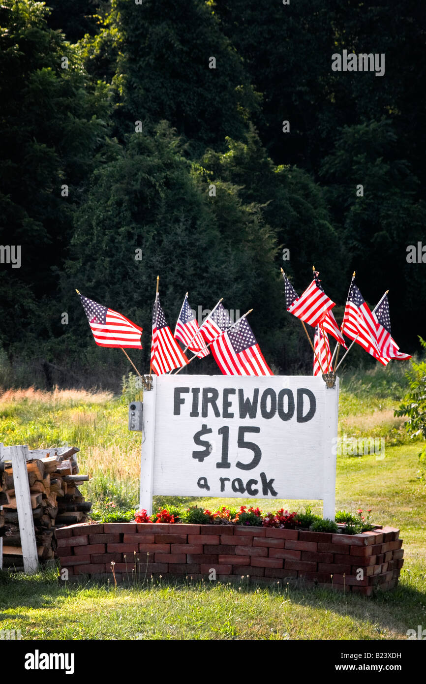 Group of American flags near firewood for sale sign, blowing in the