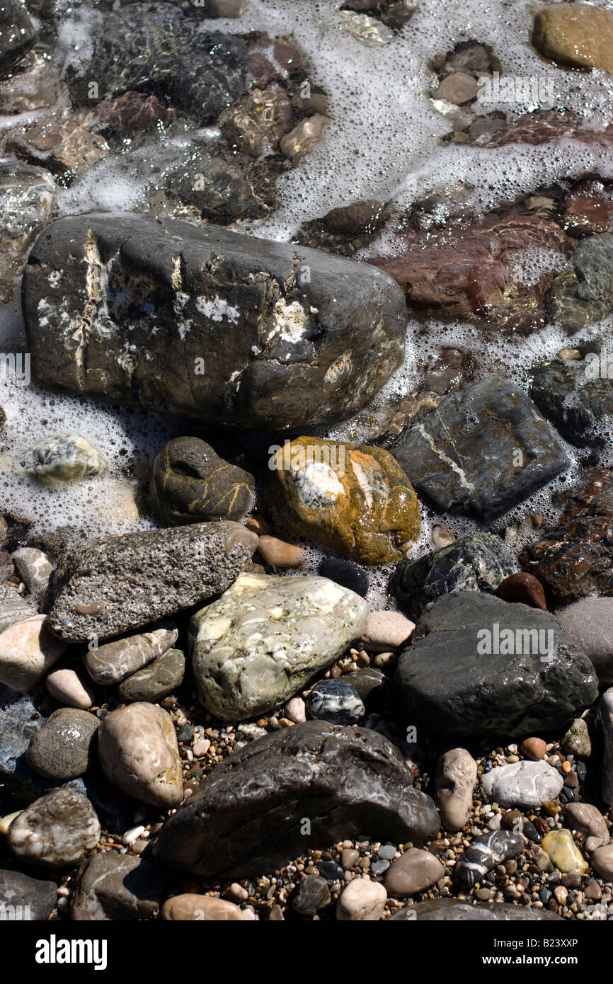 Sea waves splashes onto stoney boulder rocks on beach bay and cliffs Stock Photo