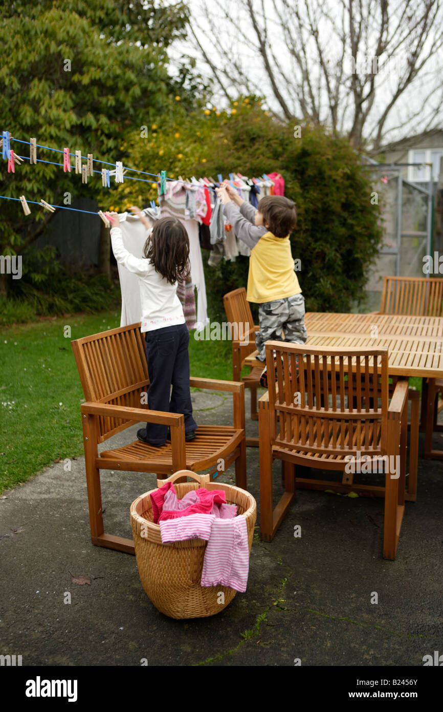 Hanging laundry on washing line to dry girl aged five and brother six standing on chair to reach high up Stock Photo