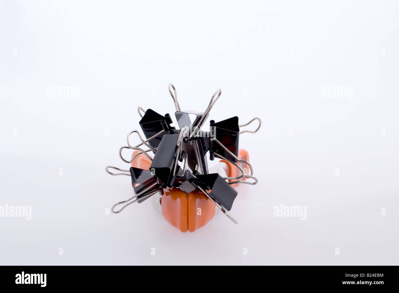 Black binder clips joined together atop a orange metal studio clip Stock Photo