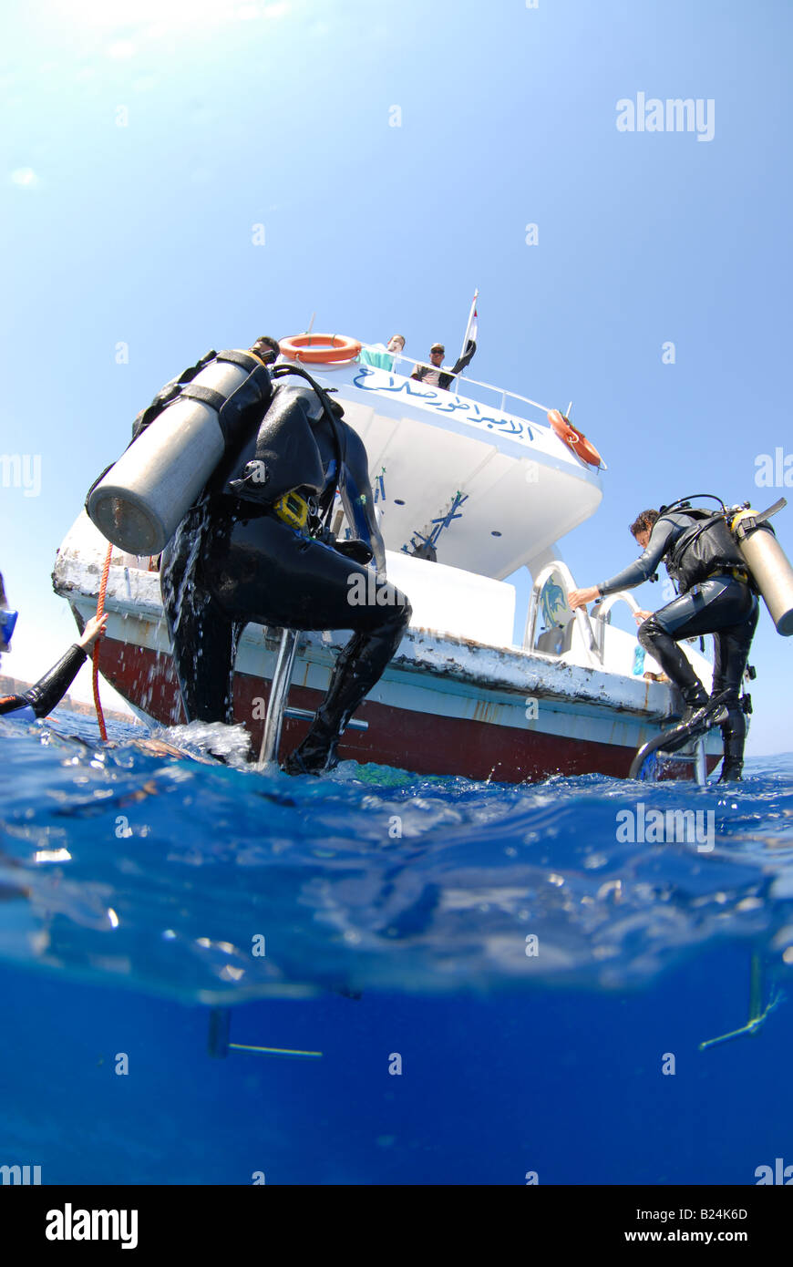 Scubadivers climbing up the boat ladder after the dive Stock Photo