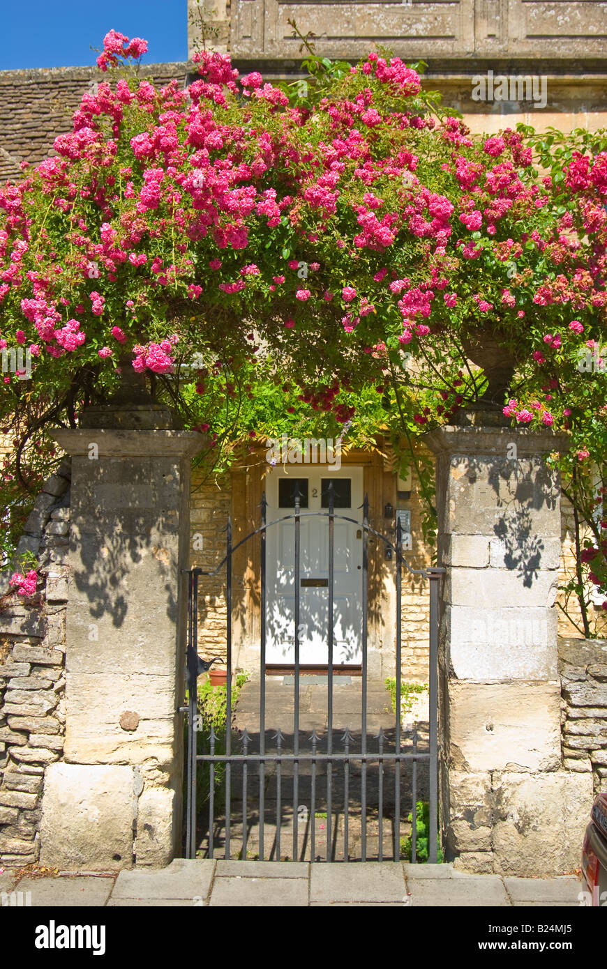 Pink rambler rose surmounting a metal gate and stone entrance to a personal property in England Stock Photo