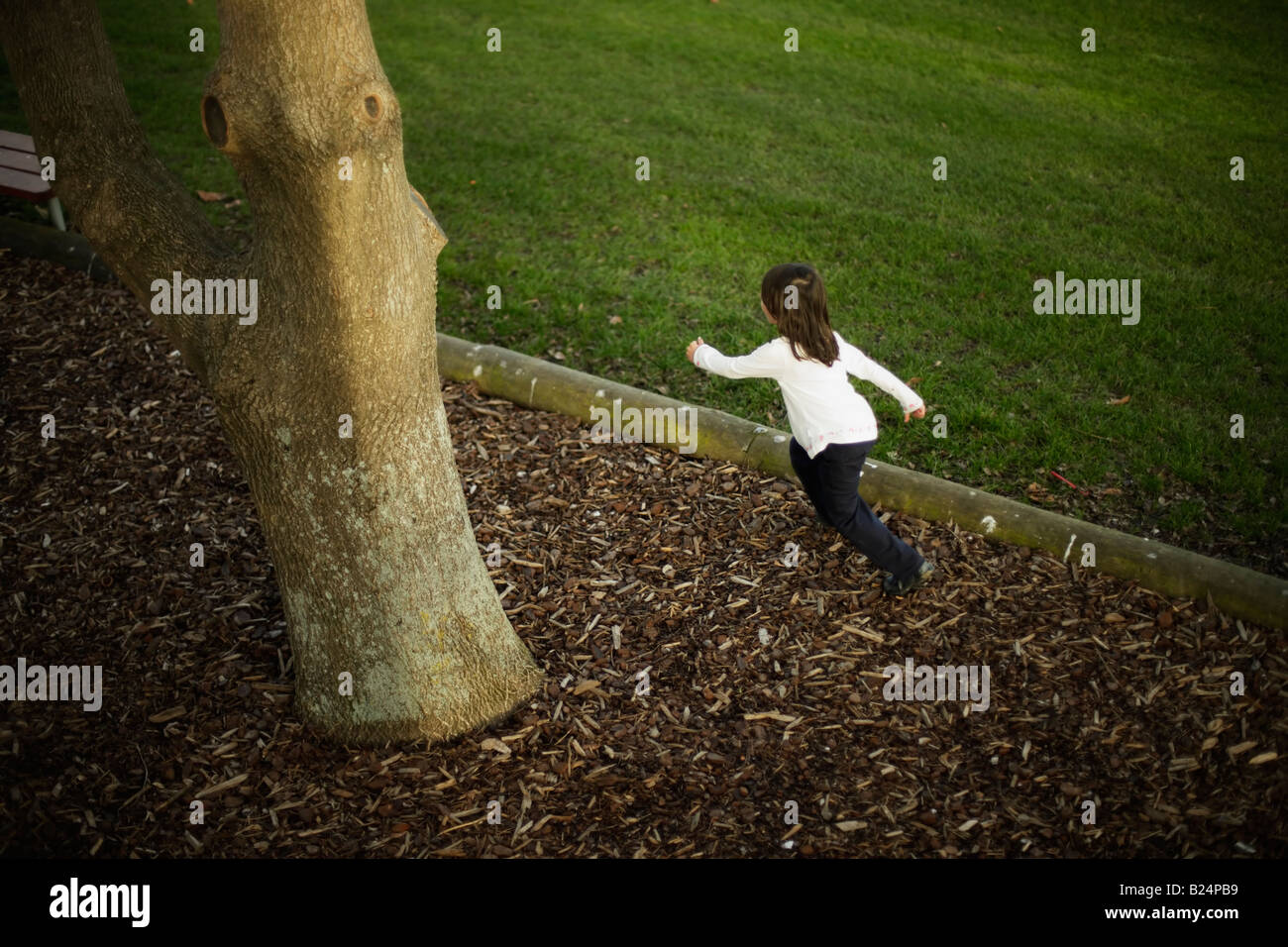 Girl aged five runs after friends in game of hide and seek Bark chippings and field at adventure playground Stock Photo