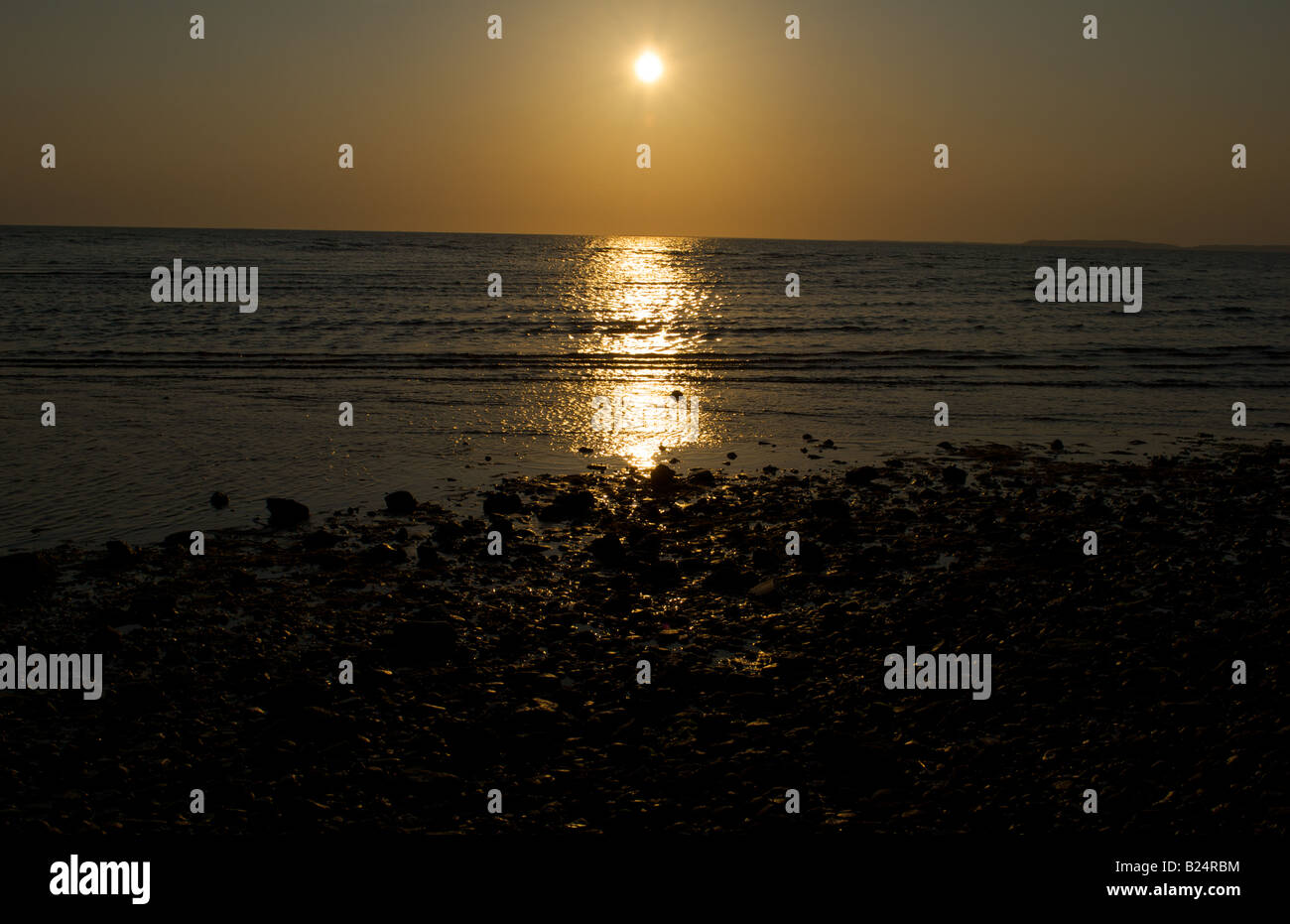 sun setting above the water with reflections in water Stock Photo - Alamy