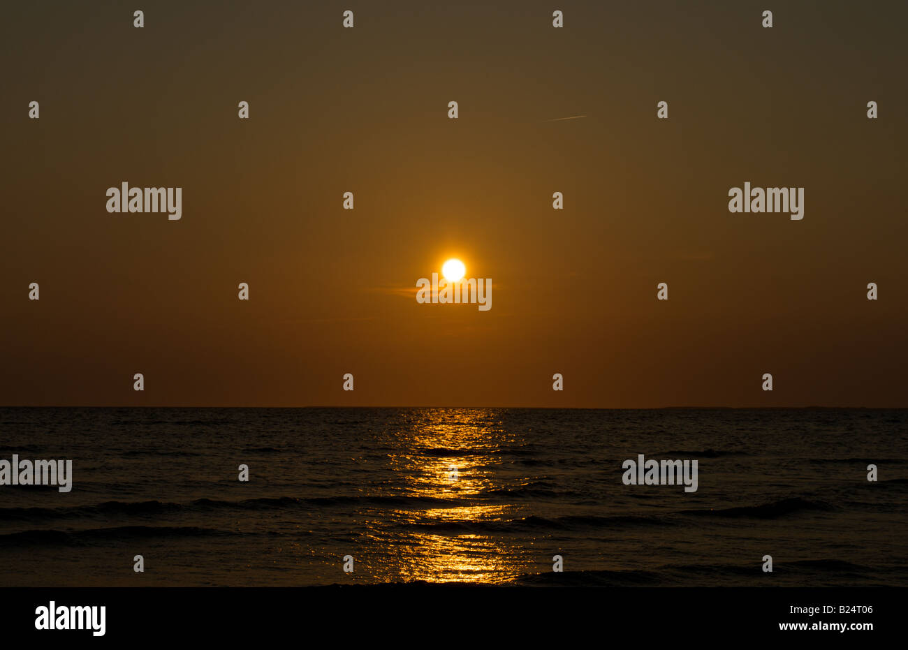 sun setting above the water with reflections in water Stock Photo - Alamy