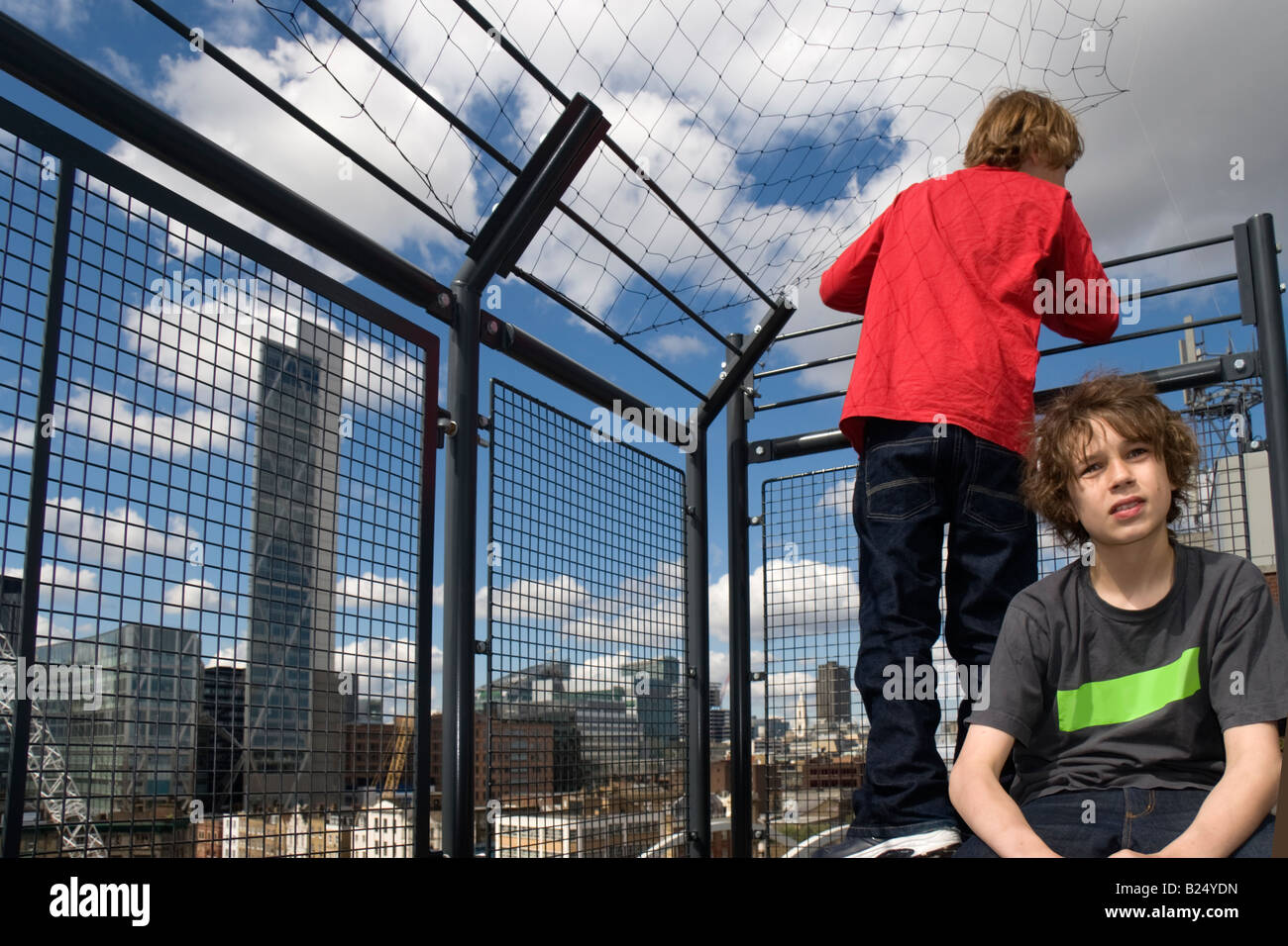 Two boys behind a protective fence on a rooftop in East London ocerlooking the City of London The Broadgate Tower designed by ar Stock Photo
