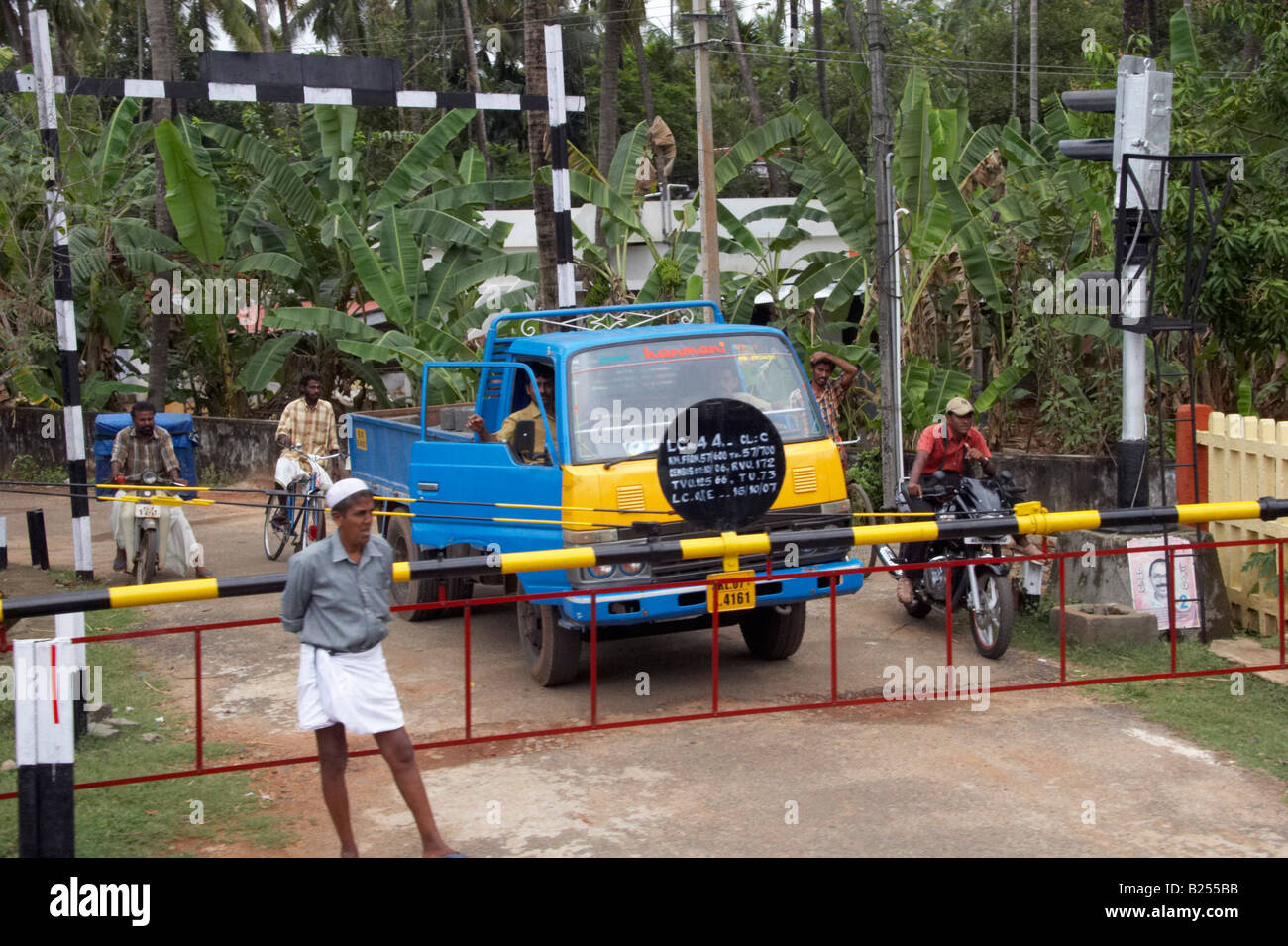 Vehicles and pedestrians wait at a level crossing near a train station between Kochi Cochin and Kannur Cannanore Kerala India Stock Photo