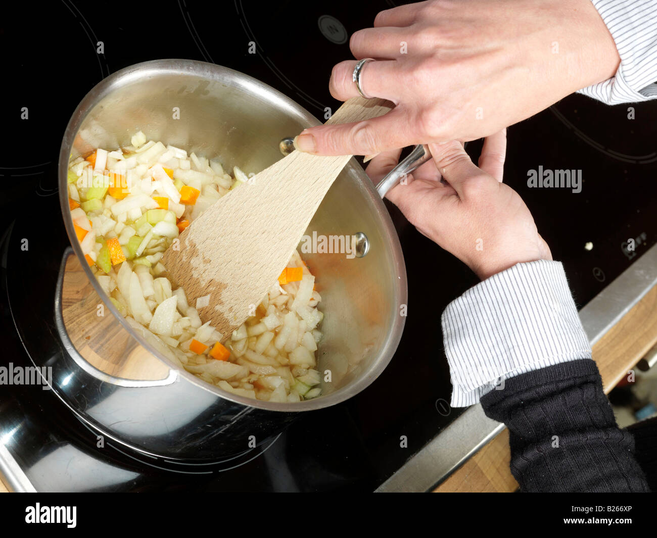 Woman Adding Freshly Diced Or Chopped Vegetables To A Saucepan Of Hot Melted Butter Preparing Italian Style Lasagne Stock Photo