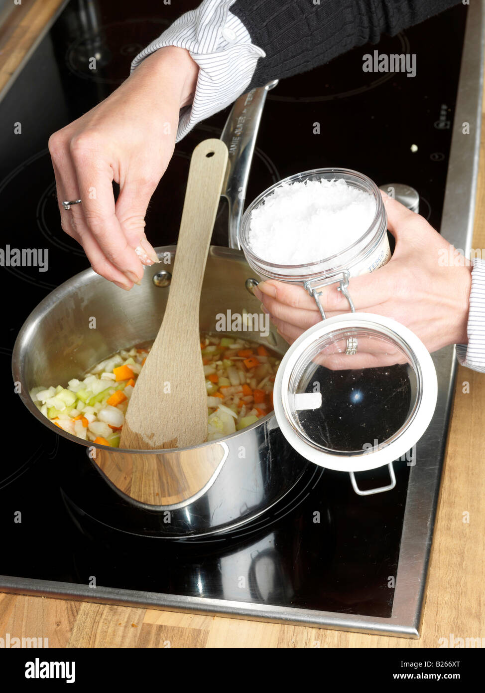 Woman Adding Freshly Diced Or Chopped Vegetables To A Saucepan Of Hot Melted Butter Preparing Italian Style Lasagne Stock Photo