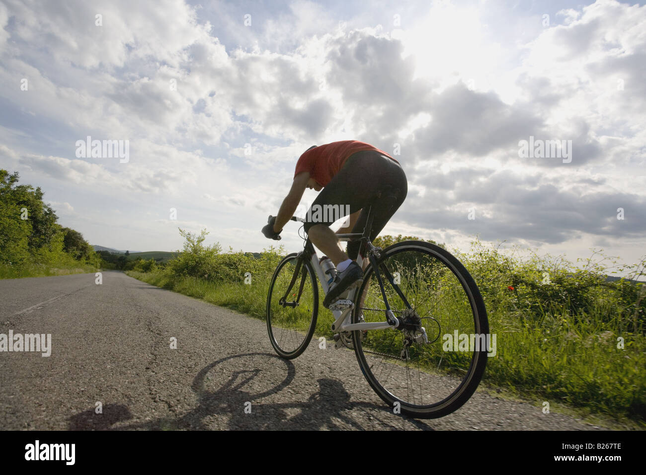 Rear view of a man cycling on road with cloudy sky Stock Photo