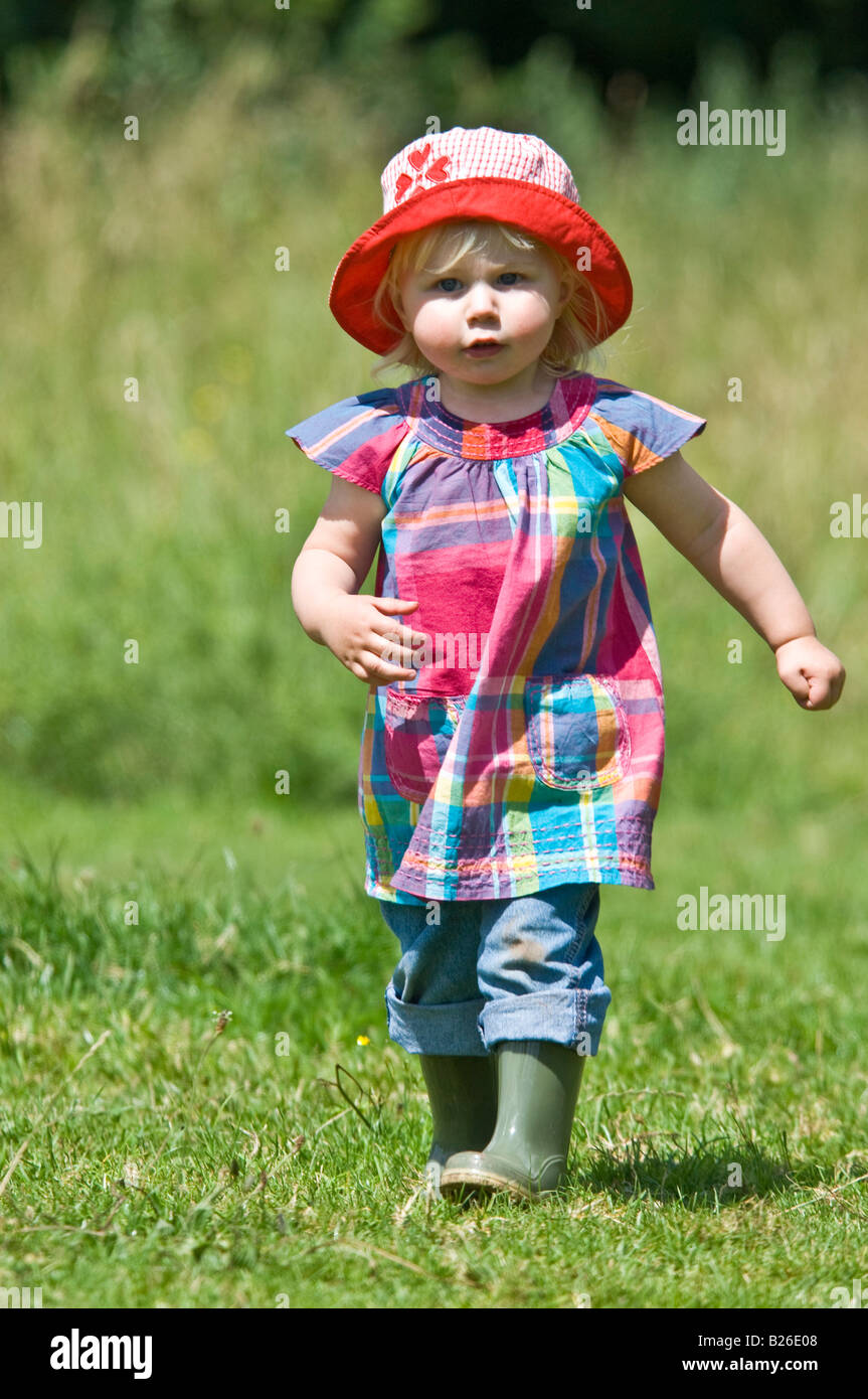 A cute young girl toddler running walking wearing wellies and a red sun