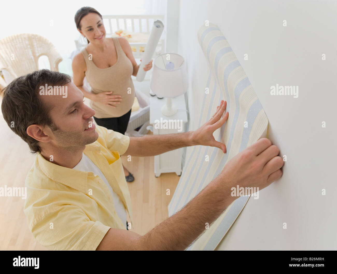 Pregnant Hispanic couple hanging wall paper in nursery Stock Photo