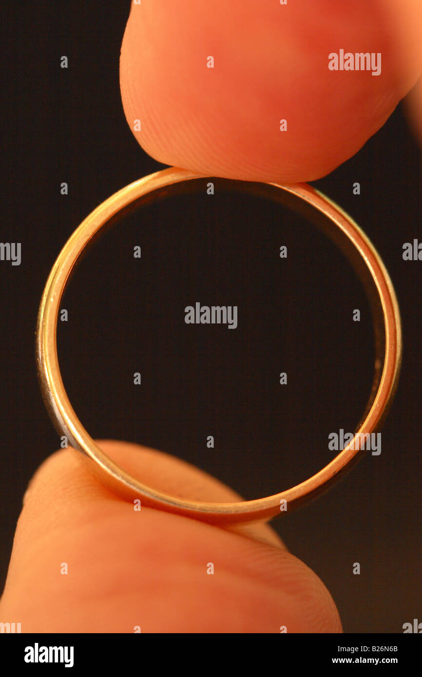 Gold golden wedding ring marriage concept held between fingers Stock Photo