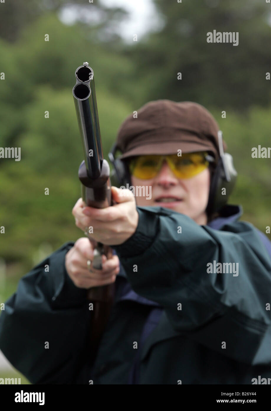Woman shooting clay pigeon targets with double barrel shotgun wearing