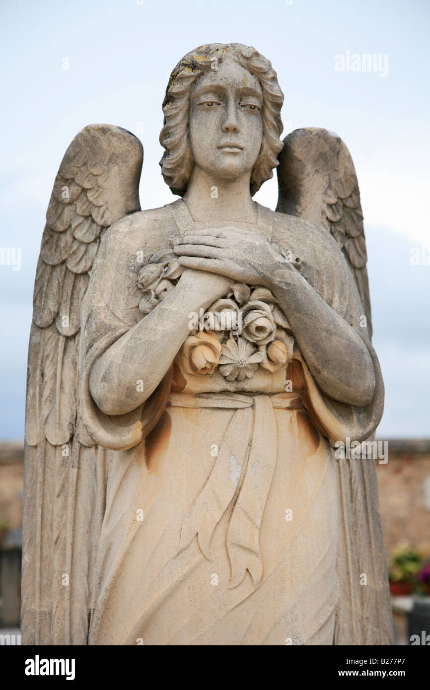 Statue of a female angel made of orange colored stone The angel is holding a bouquet of flowers against her chest. Stock Photo