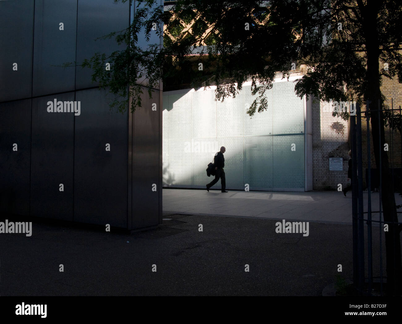 Silhouette of office worker with a satchel over his shoulder walking through a beam of light. South Bank, London July 2008 Stock Photo