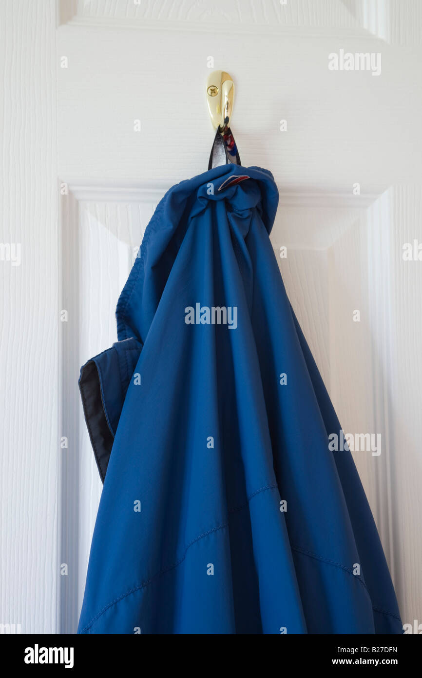 Blue coat jacket hanging on a hook on back of white wooden door. England UK Stock Photo