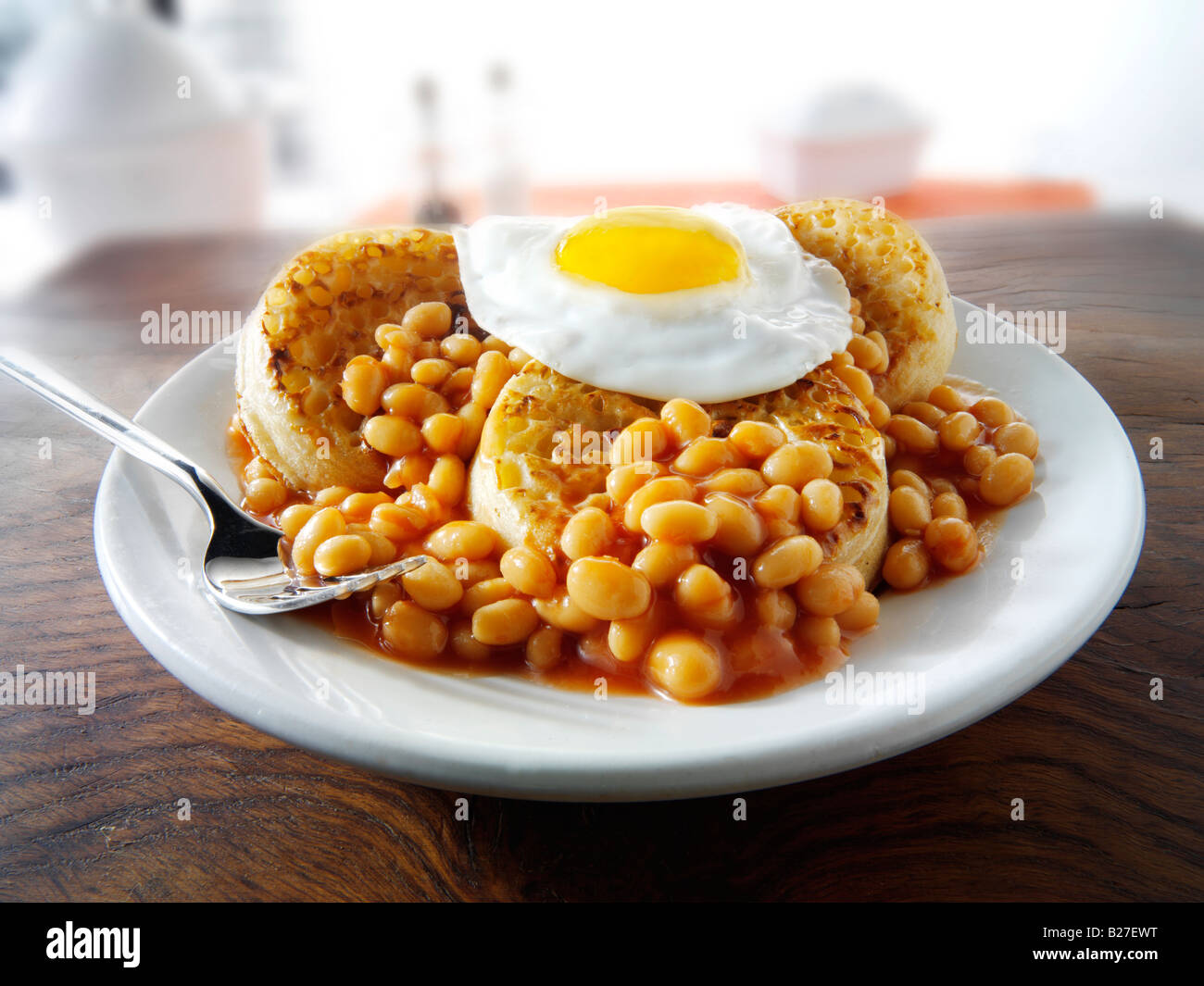 Baked beans and a fried egg on crumpets served as a meal on a white