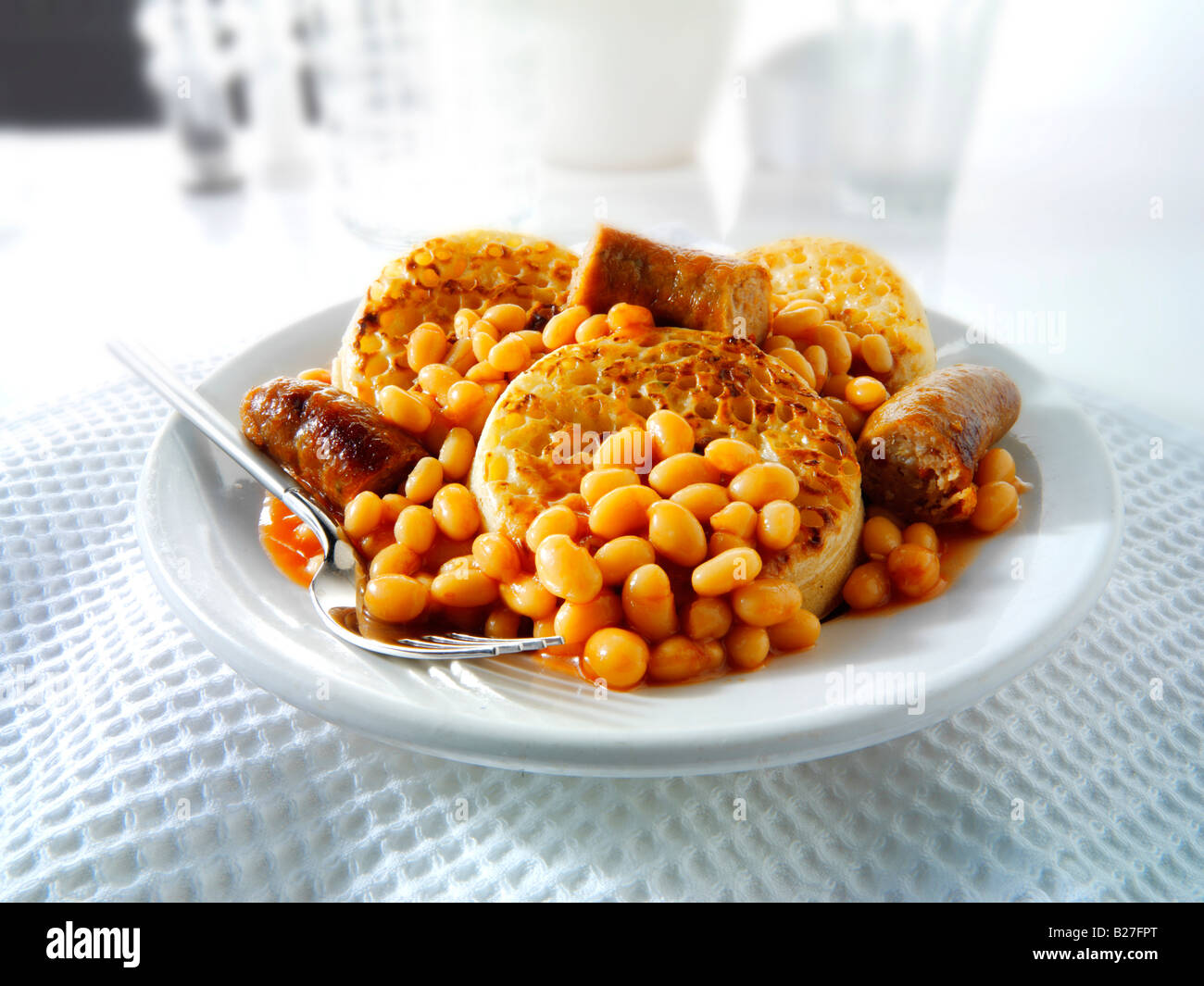 Baked beans and sausages on crumpets served as a meal on a white plate in a table setting Stock Photo