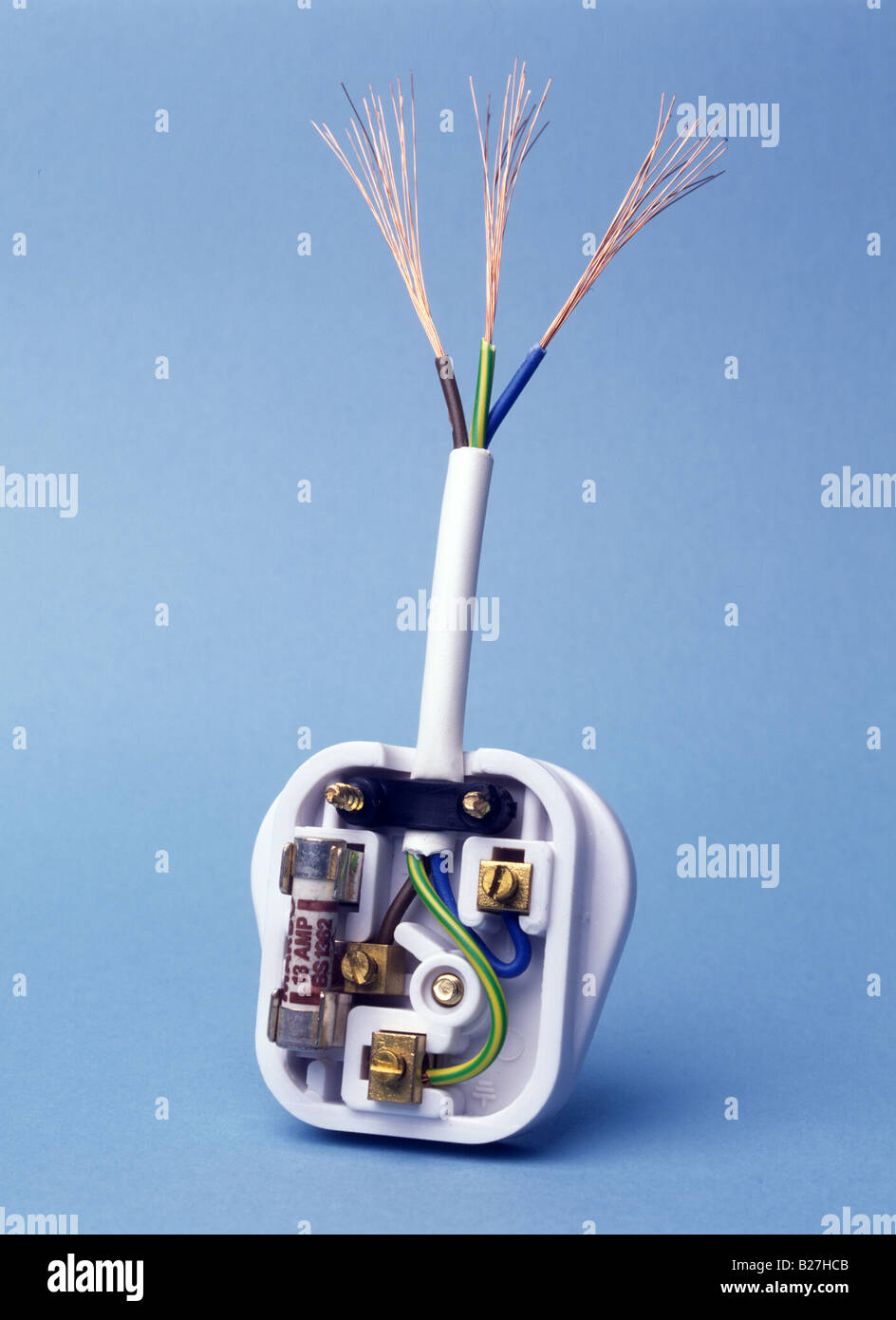 3 pin plug UK type showing copper wires and insulation blue neutral brown live green and yellow earth on blue background Stock Photo