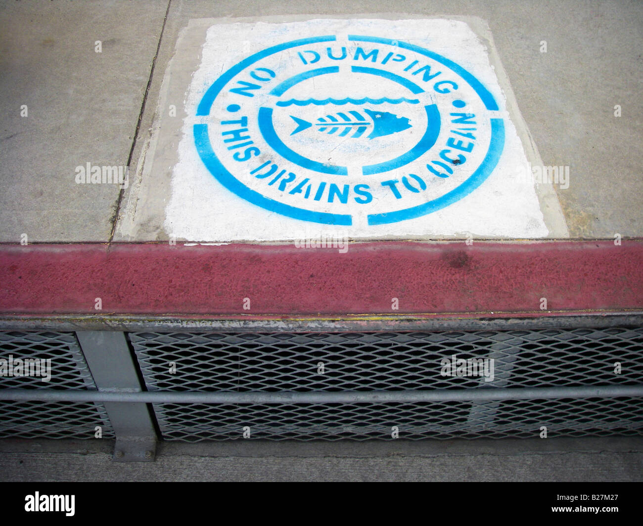 A storm drain near the ocean with sign declaring not to dump waste, as it will flow into the sea. Stock Photo
