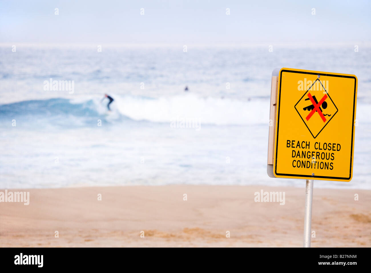 Bronte Beach in winter with few surfers and sign reading: Beach Closed Dangerous Conditions. Stock Photo