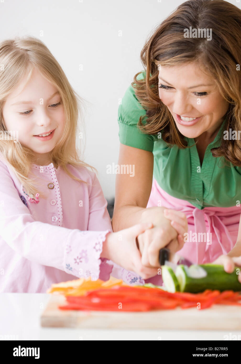 Mother helping daughter chop vegetables Stock Photo