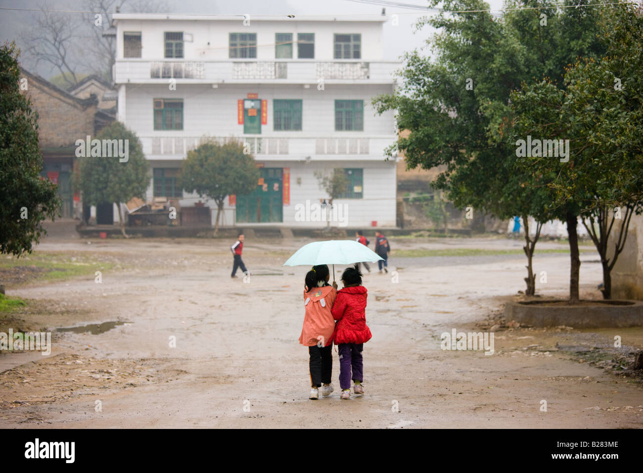 Young girls share an umbrella after leaving school in Fuli China has a one child policy to limit population Stock Photo