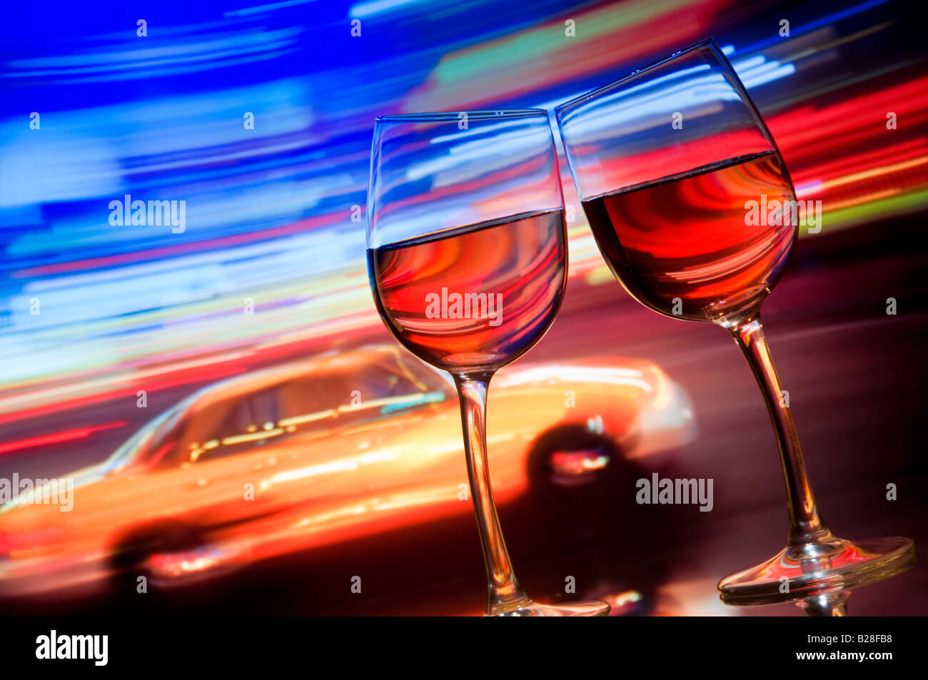 Two wine glasses lean together with blurred yellow taxi cab and streaks of neon lighting behind. Times Square New York City USA Stock Photo