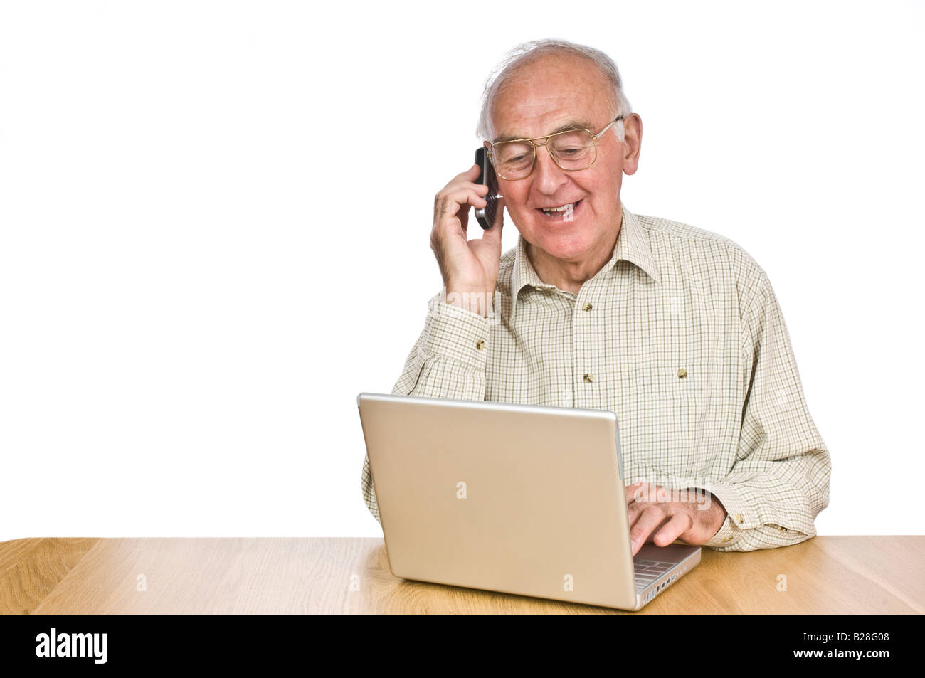 An elderly man at a desk with a lap top computer while talking on a mobile phone against a pure white (255) background. Stock Photo