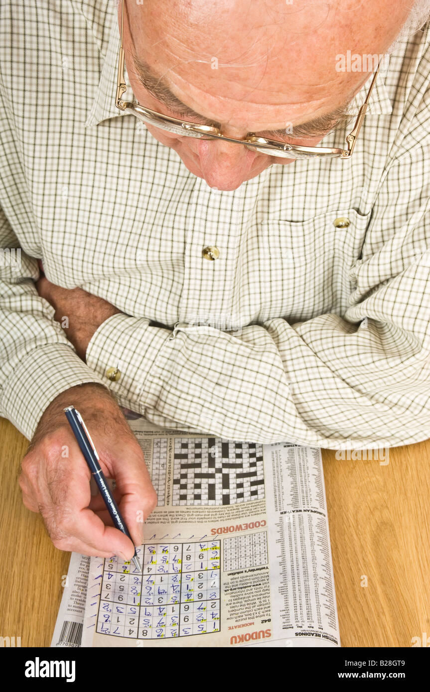 An elderly man concentrating on a sudoku puzzle in a newspaper. Stock Photo