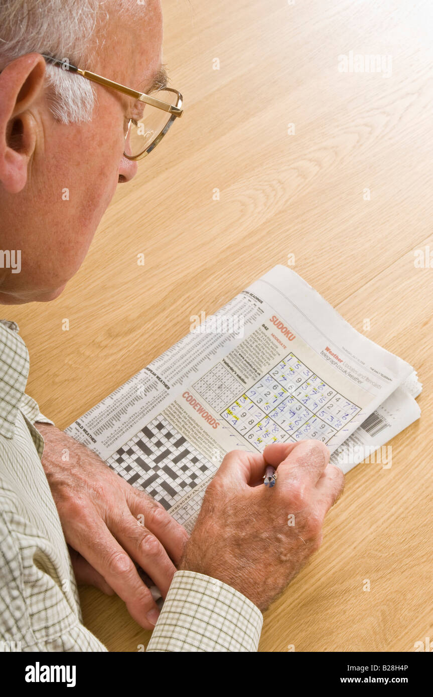 An elderly man concentrating on a sudoku puzzle in a newspaper. Stock Photo