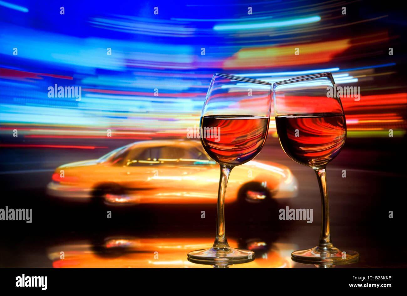 Two wine glasses lean together with blurred yellow taxi cab and streaks of neon lighting behind. Times Square New York City USA Stock Photo