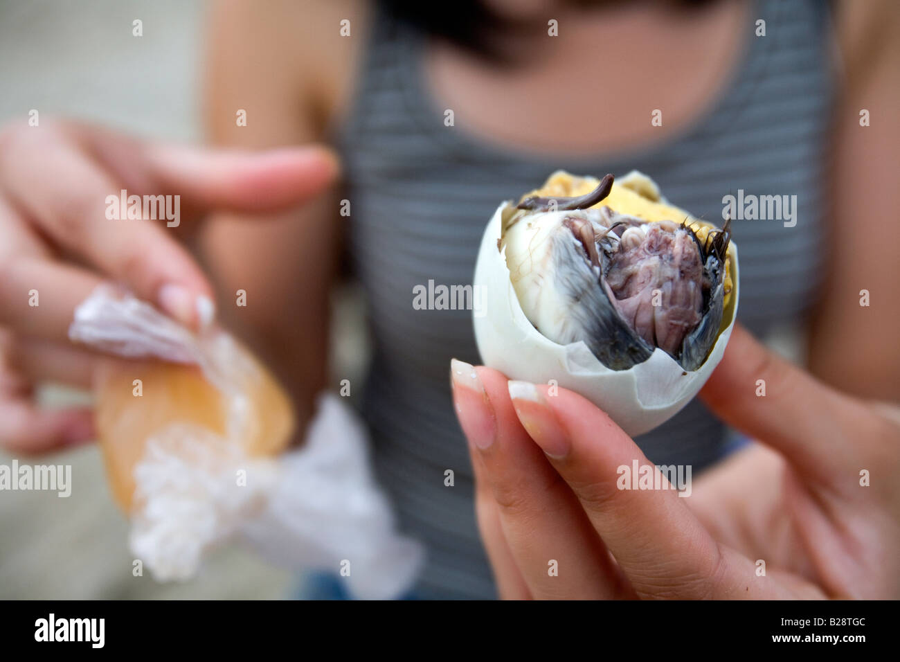 A Filipina eats a balut with vinegar on White Beach in Puerto Galera, Philippines. Stock Photo