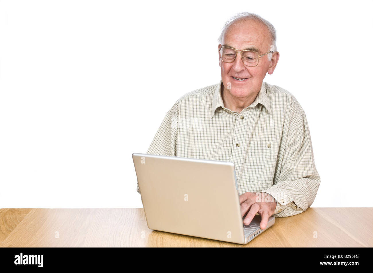 An elderly man at a desk looking at a lap top computer screen and smiling against a pure white (255) background. Stock Photo